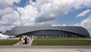 Prosklená fasáda terminálu Letiště Brno-Tuřany s nápisem BRNO a skupinou cestujících s kufry na chodníku před budovou